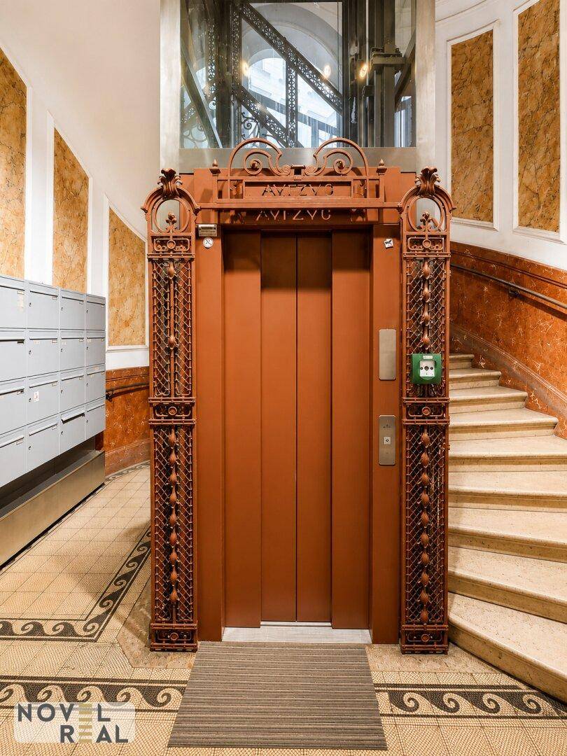 Historischer Aufzug mit kunstvoller Metallverzierung in einem eleganten Treppenhaus.