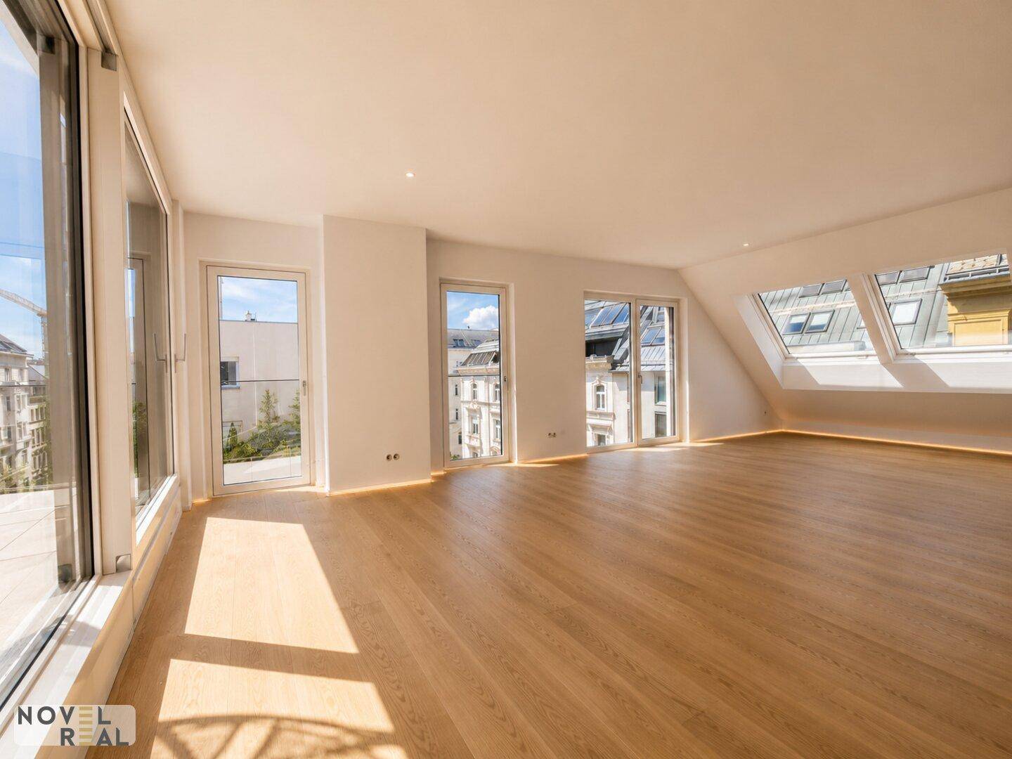 Heller Wohnraum im Dachgeschoss mit Holzfußboden, Dachfenstern und Blick auf die Stadt.