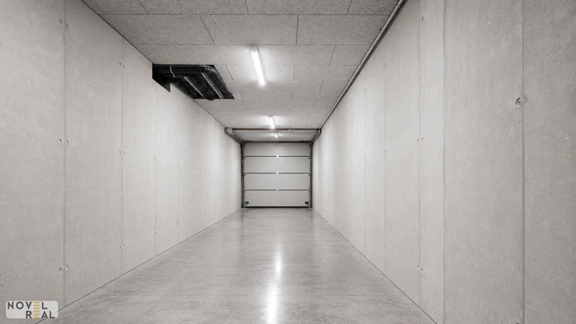 Langer Gang in einer Tiefgarage mit Rolltor am Ende und Betonwänden.
