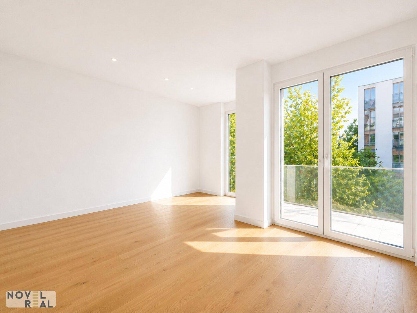 Lichtdurchfluteter Raum mit Holzboden und Zugang zu einem Balkon, umgeben von Grün.
