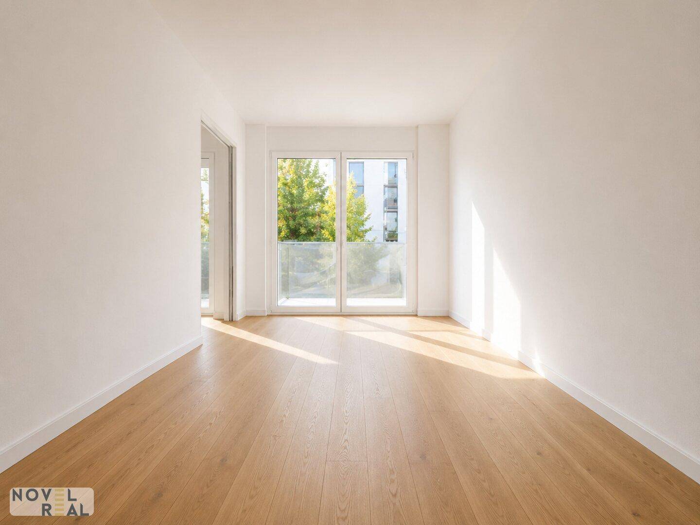 Sonniger Raum mit Holzboden und großen Fenstern, die einen Blick ins Grüne bieten.