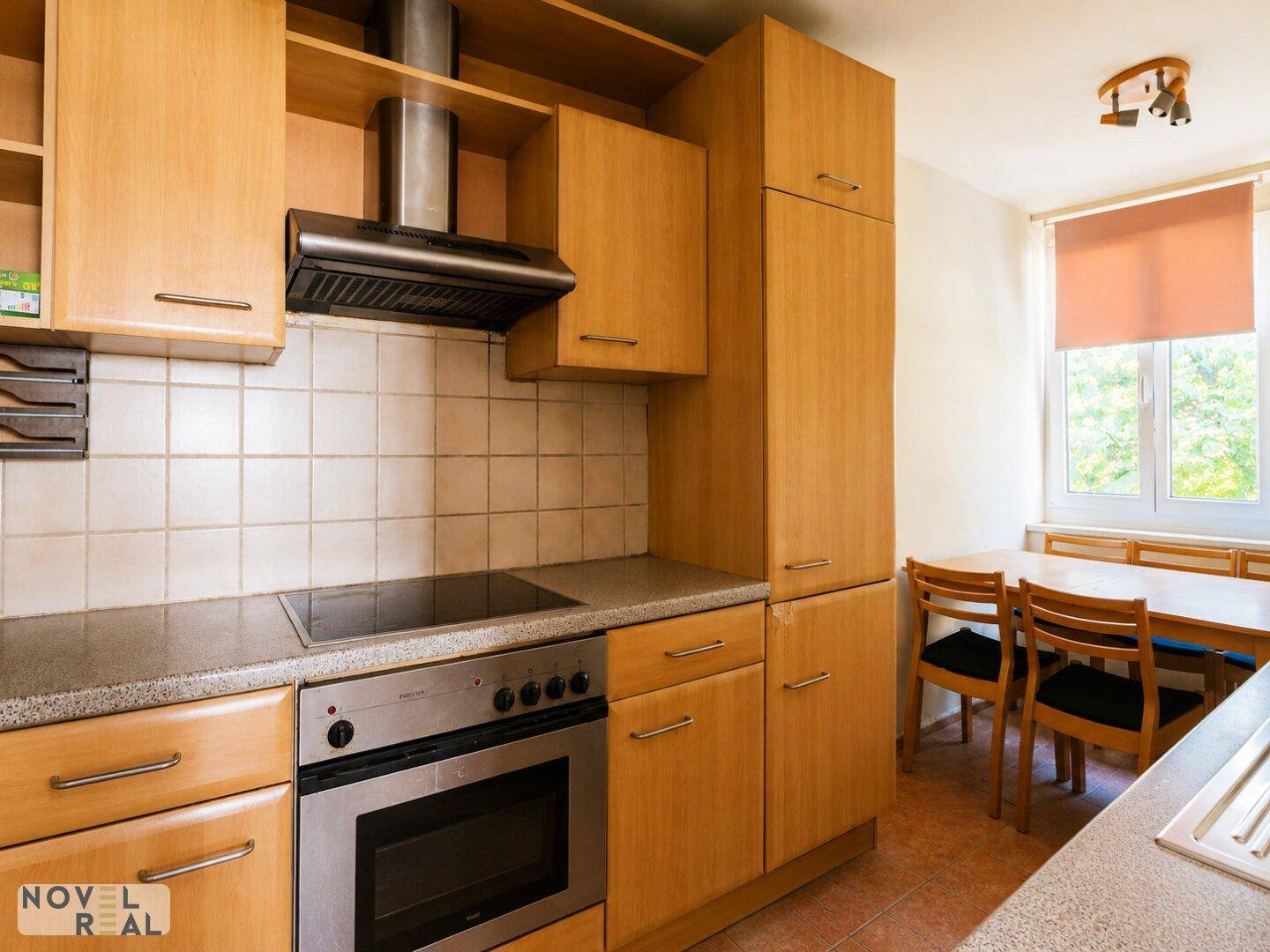 Funktionale Küche mit Holzschränken, Fliesenrückwand und Essbereich am Fenster.