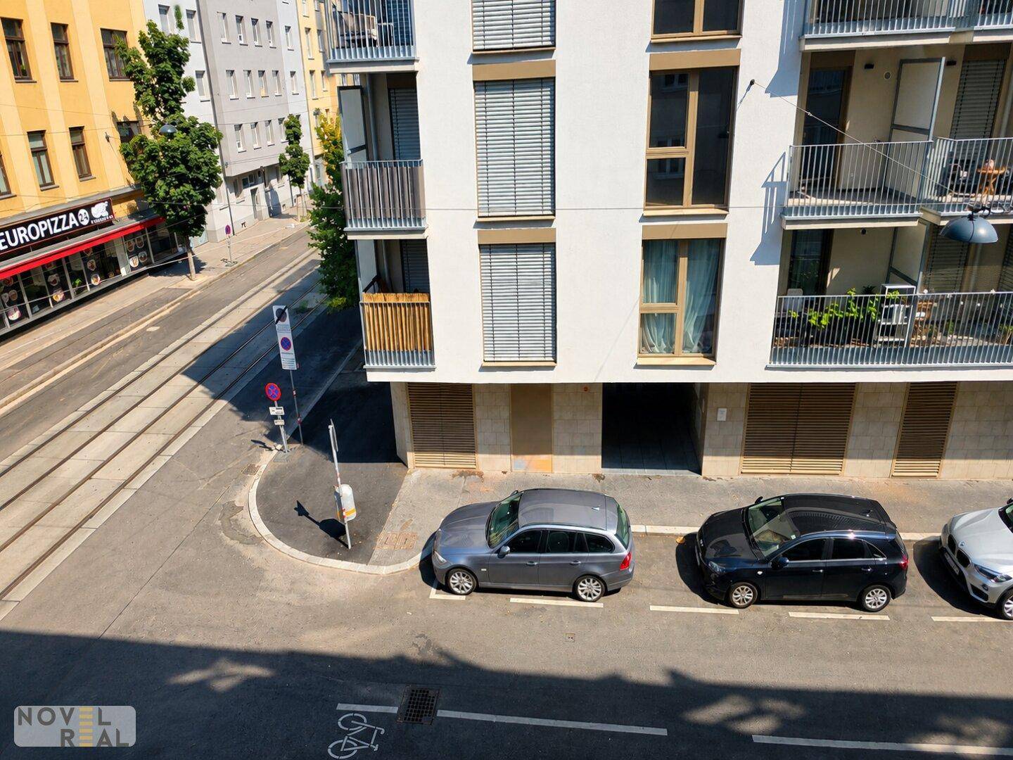 Straßenansicht mit parkenden Autos, Straßenbahnschienen und Wohngebäuden im Hintergrund.