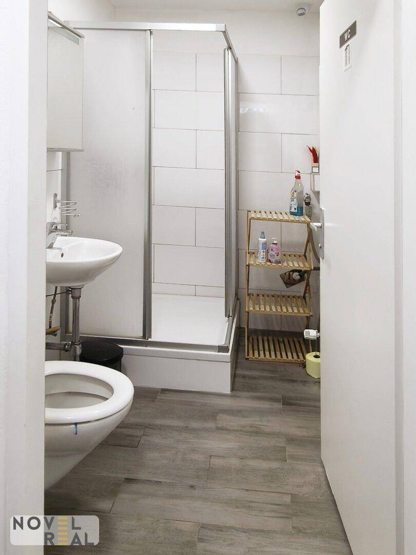 Badezimmer mit Toilette, Waschbecken, Duschkabine und Fliesenboden in Holzoptik.