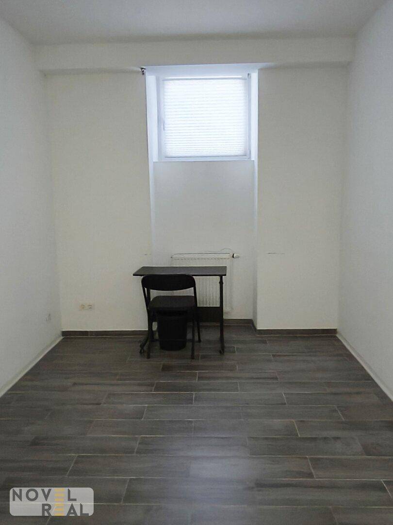 Heller, leerer Raum mit Fliesenboden in Holzoptik, weißen Wänden und einem Fenster mit Jalousien.
