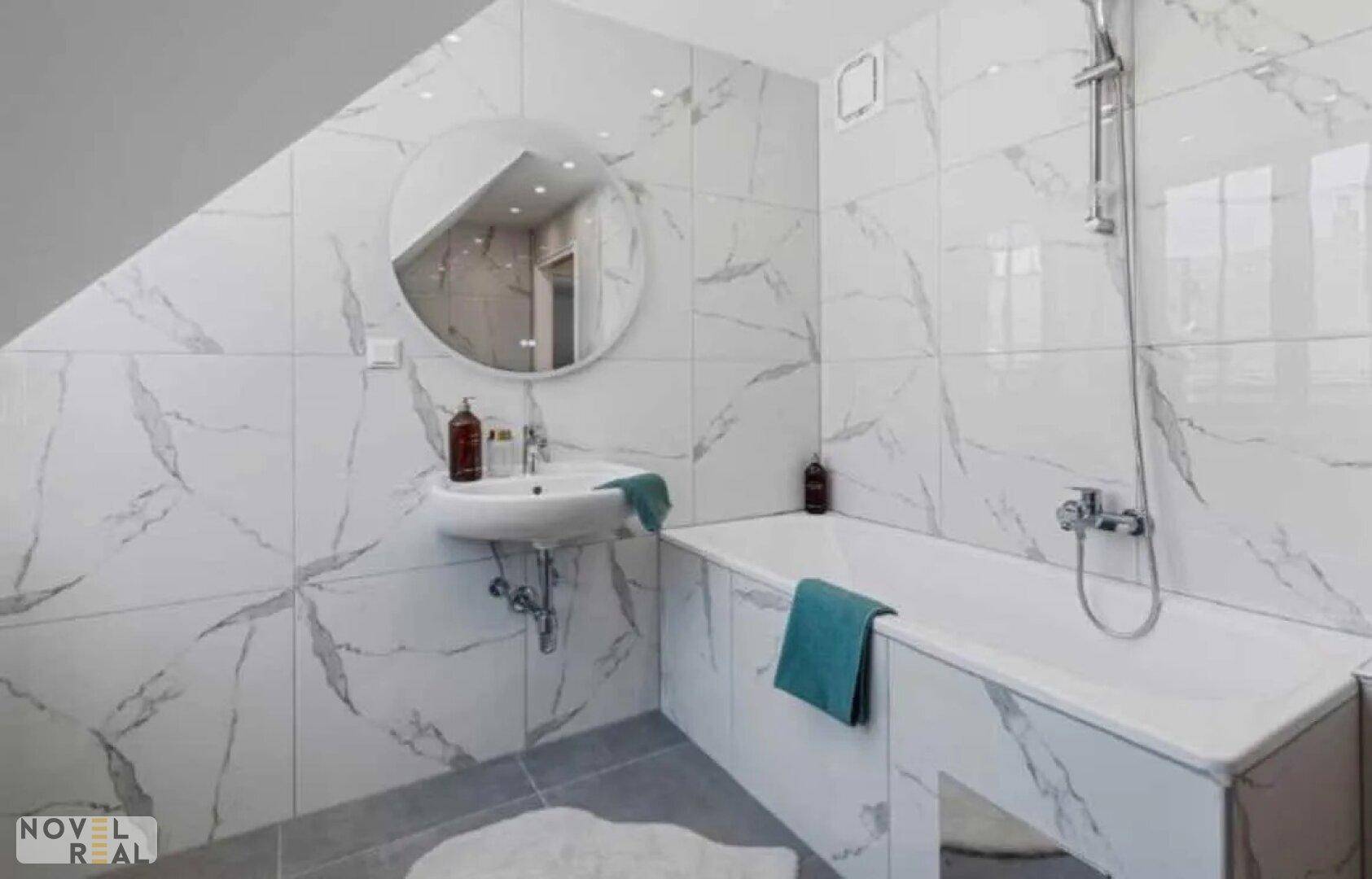 Helles Badezimmer mit Badewanne, Waschbecken und modern gefliesten Wänden.