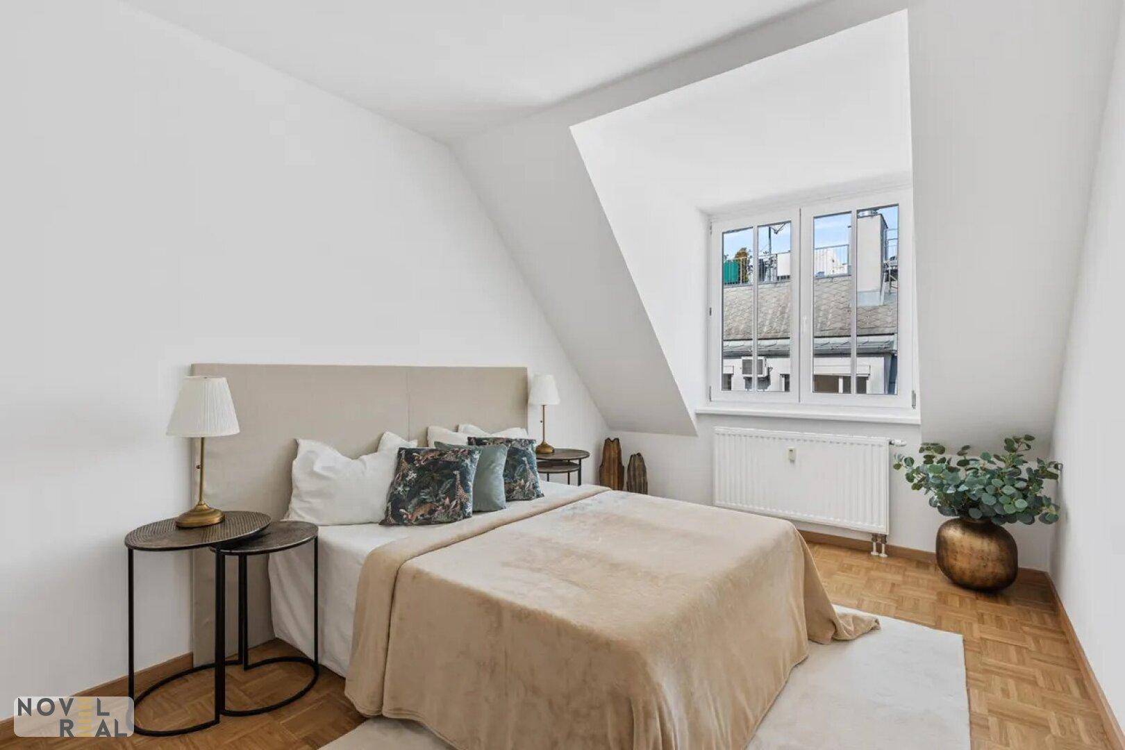 Helles Schlafzimmer mit Dachschräge, Parkettboden und einem großen Fenster.