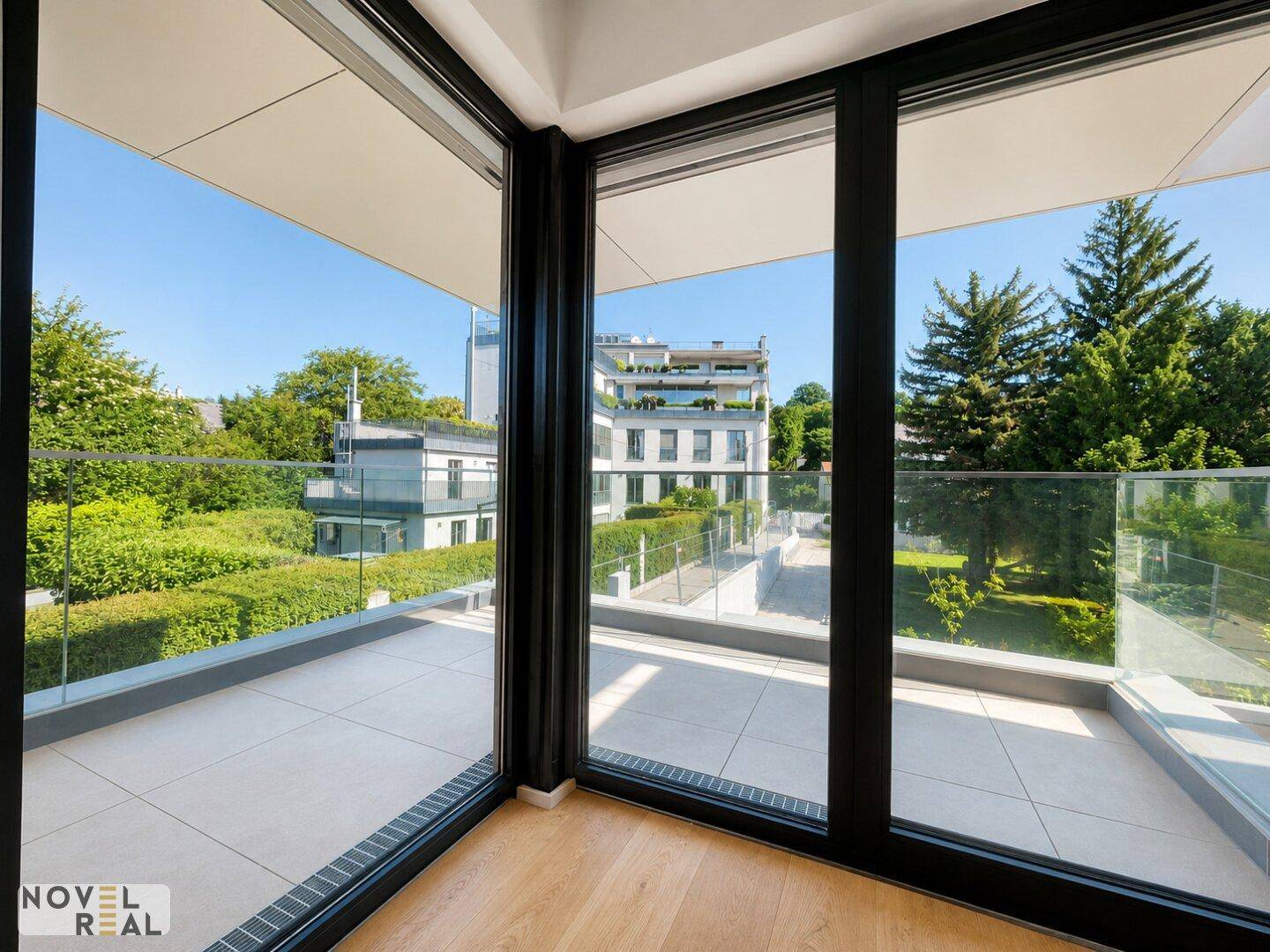 Heller Innenraum mit großen Fenstern und Zugang zu einem Balkon mit Blick auf die grüne Umgebung.