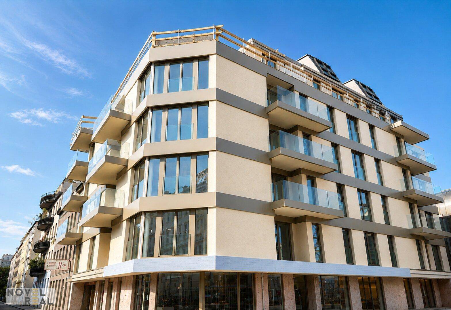 Eckgebäude mit moderner Architektur, Glasbalkonen und großen Fensterfronten im Erdgeschoss.