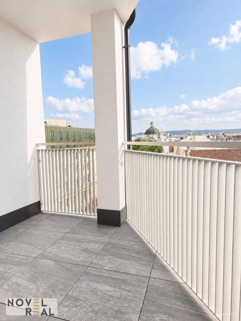 Heller Balkon mit Fliesenboden, weißem Geländer und weitem Blick über die Stadt.