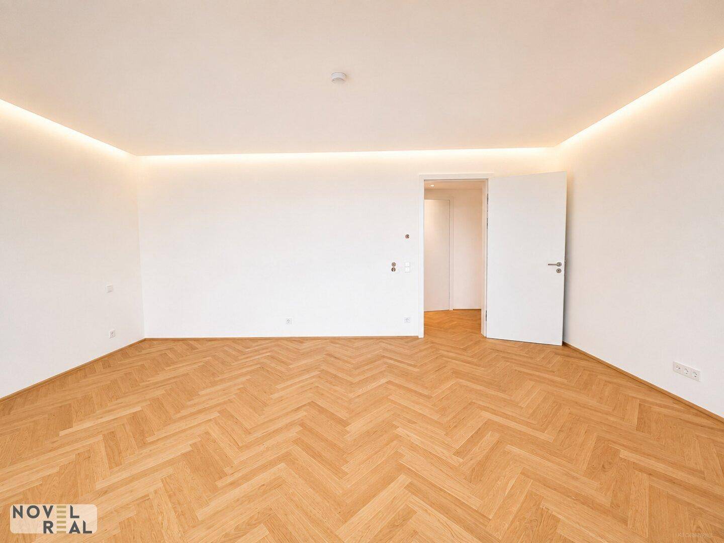Geräumiges Schlafzimmer mit Fischgrätparkett, weiß gestrichenen Wänden und Zugang zu einem weiteren Raum.