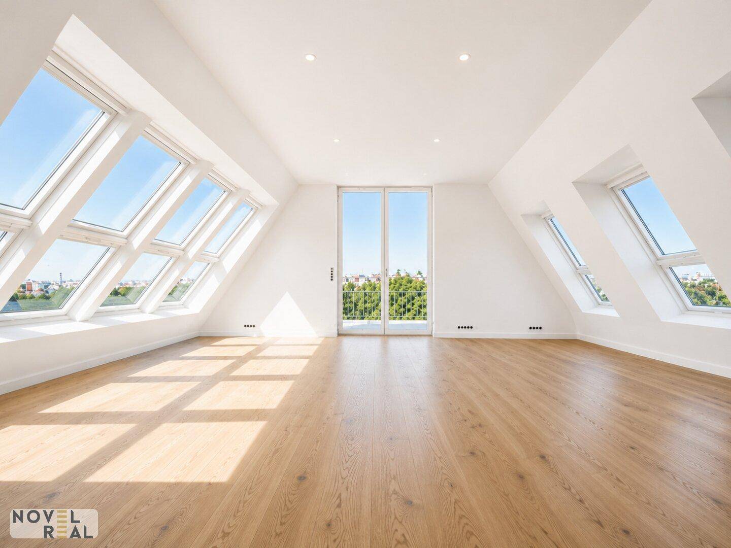 Lichtdurchfluteter Dachgeschossraum mit vielen Dachfenstern, Holzboden und Zugang zu einem kleinen Balkon.