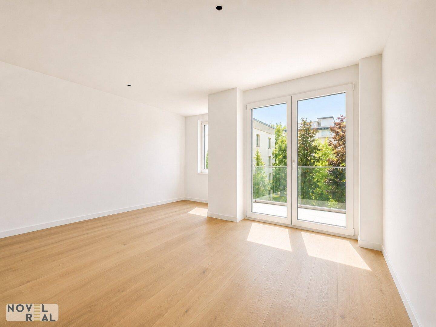 Geräumiges, helles Zimmer mit Holzboden und großen Fenstern, die viel Tageslicht hereinlassen.
