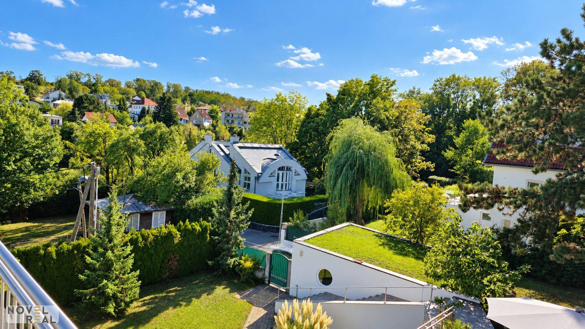 Weitläufiger Blick auf die grüne Umgebung mit Häusern und der Holzterrasse im Vordergrund.