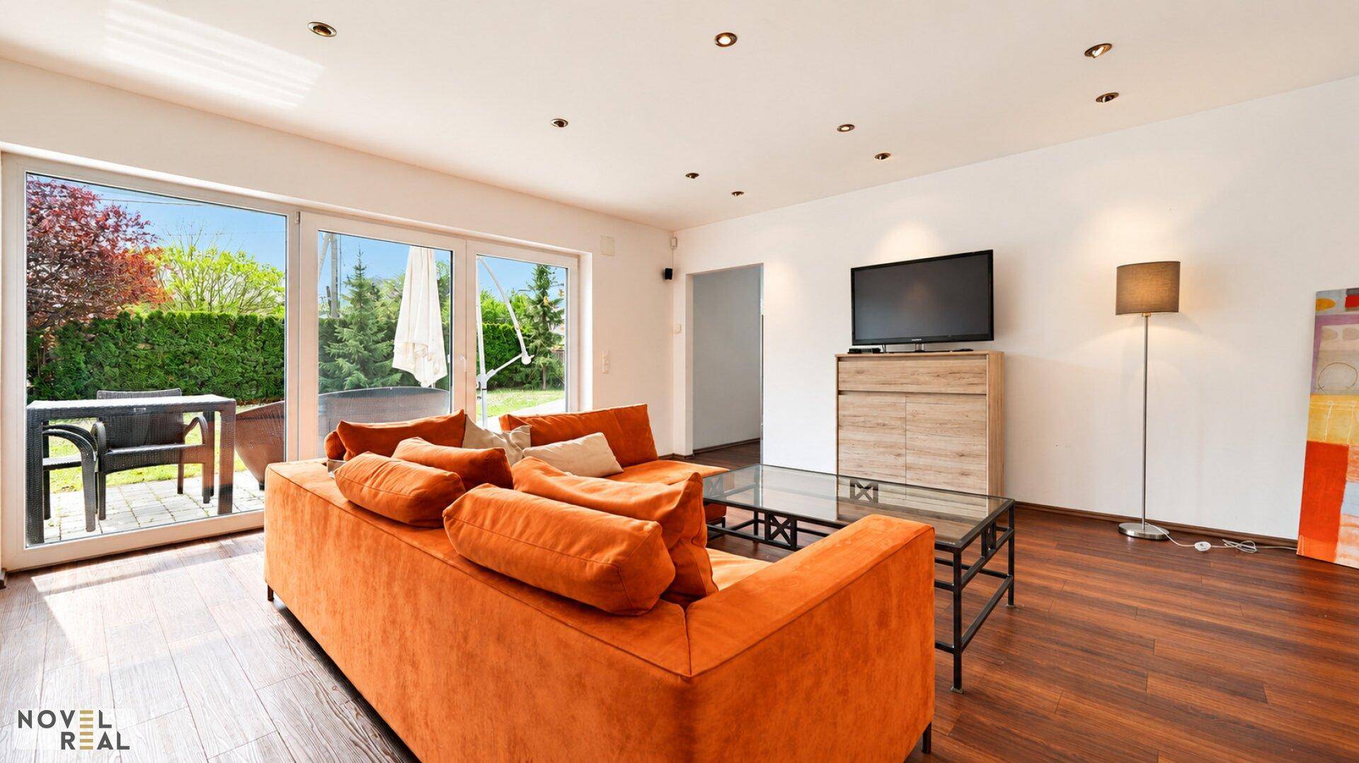 Helles Wohnzimmer mit orangefarbenem Sofa, dunklem Parkett und direktem Terrassenzugang.