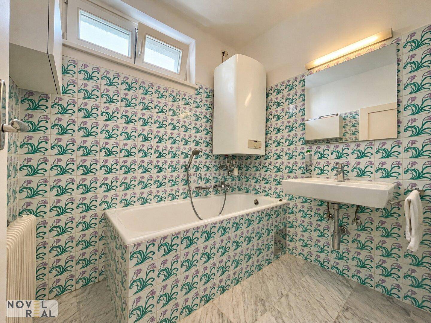 Badezimmer mit Badewanne, Waschbecken und auffälligen floralen Fliesen an den Wänden.