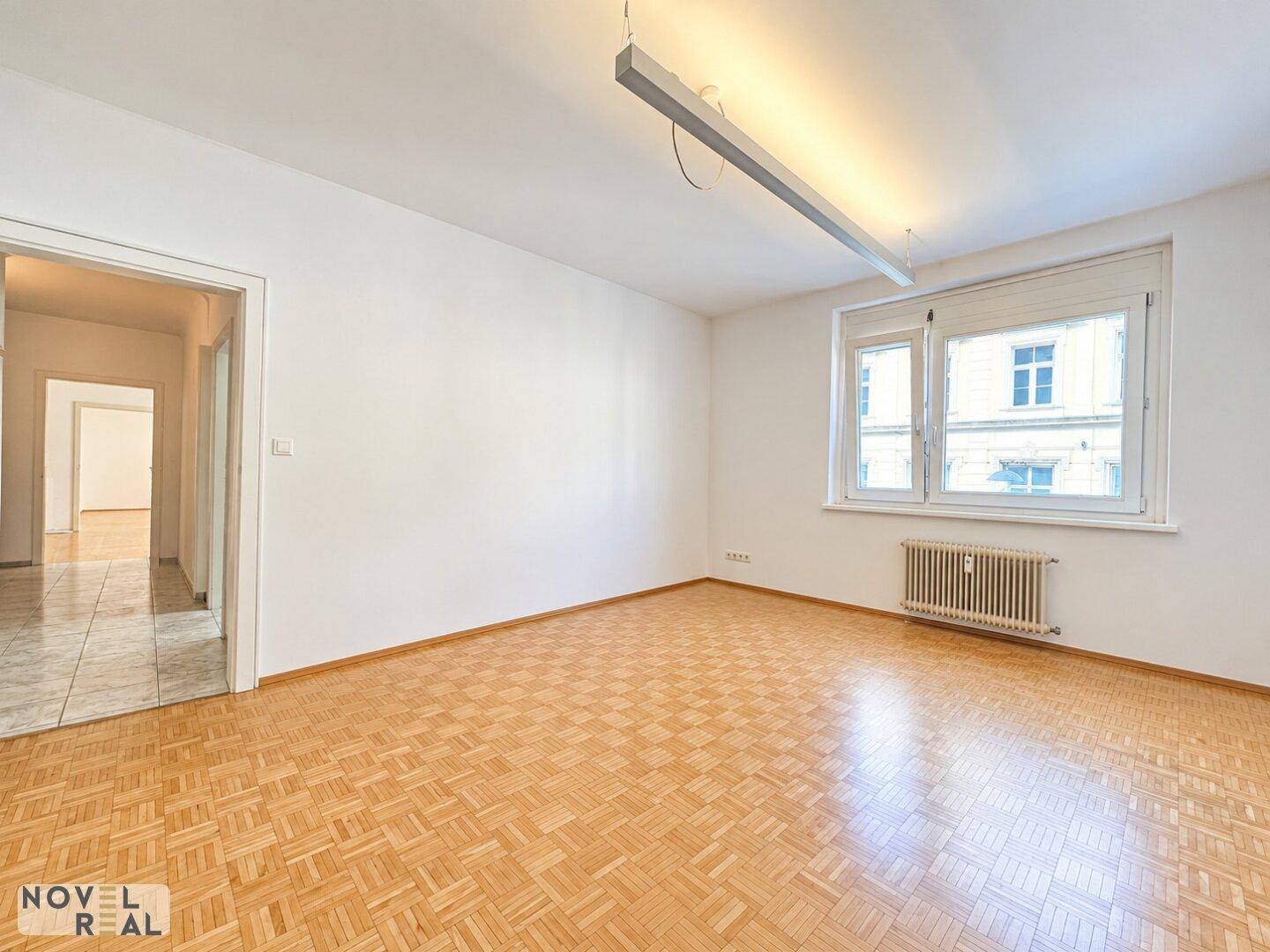 Heller Raum mit Mosaikparkettboden und Zugang zu einem weiteren Zimmer, gut beleuchtet.