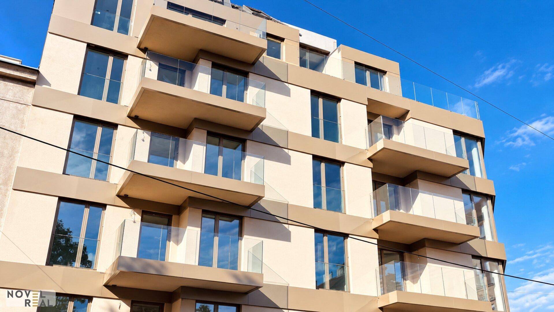 Detailansicht der modernen Gebäudefassade mit gestuften Balkonen und großen Glasflächen unter blauem Himmel.