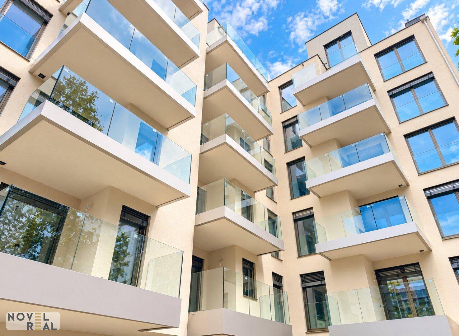 Aufwärtsblick auf die moderne Gebäudefassade mit gestaffelten Balkonen und Glasgeländern.