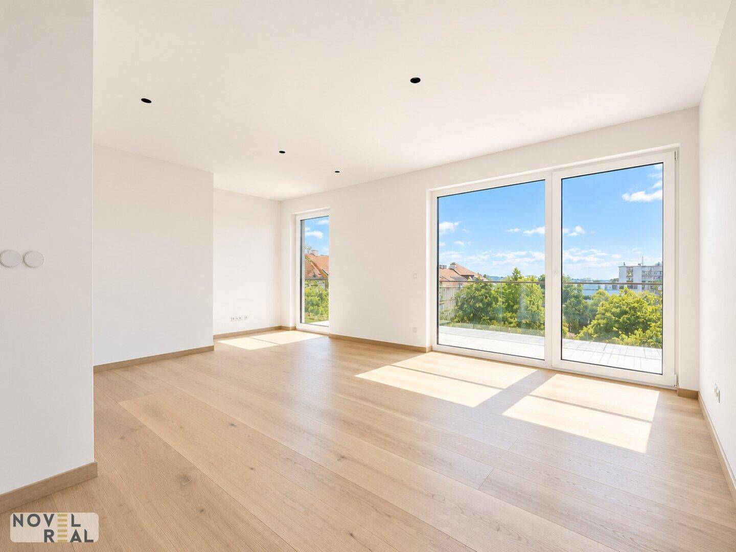 Helles, leeres Wohnzimmer mit Holzboden, großen Fenstern und Zugang zu einer Terrasse.