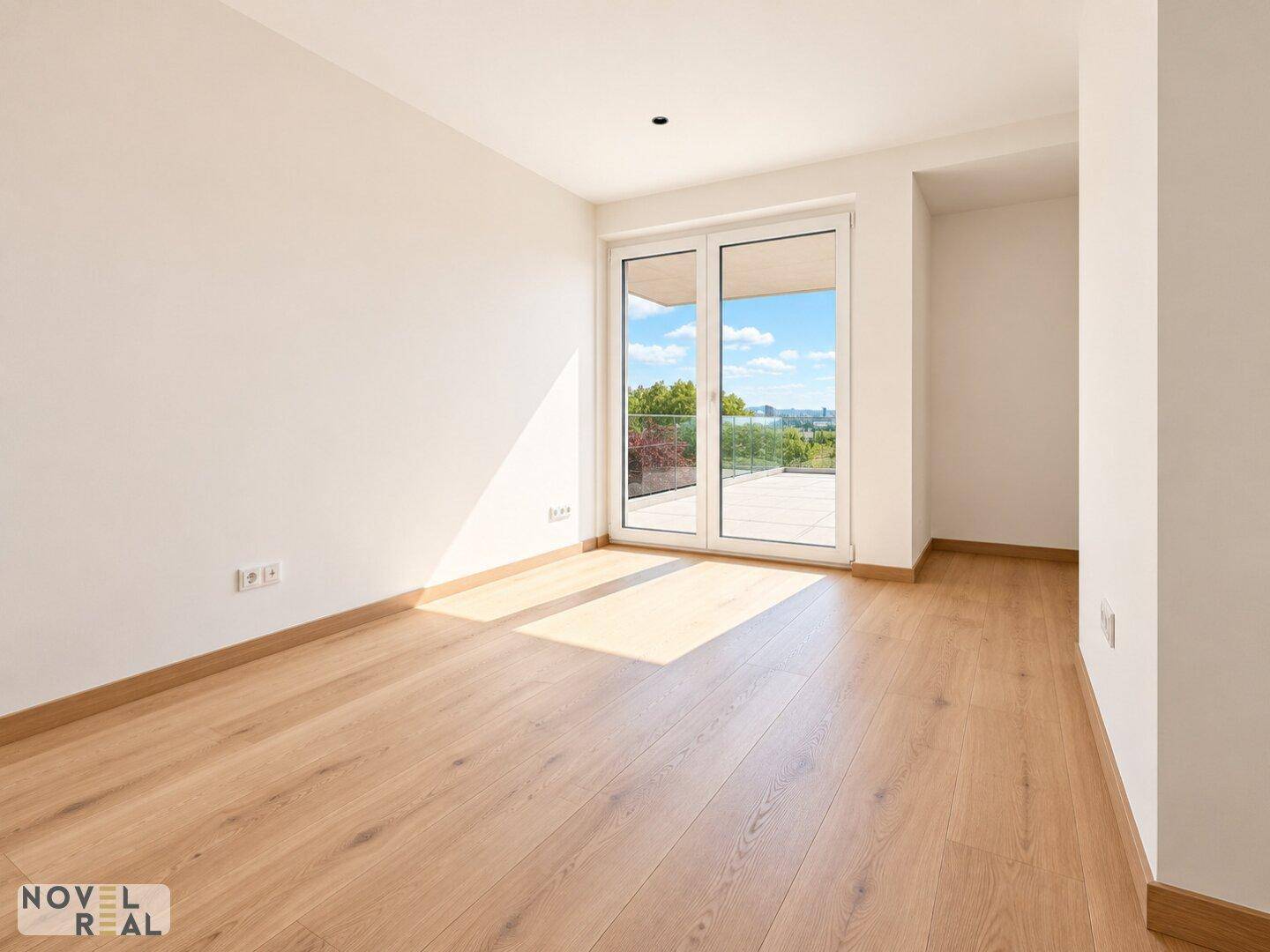 Leeres Zimmer mit Holzboden und großen Fenstern, die viel Tageslicht hereinlassen.
