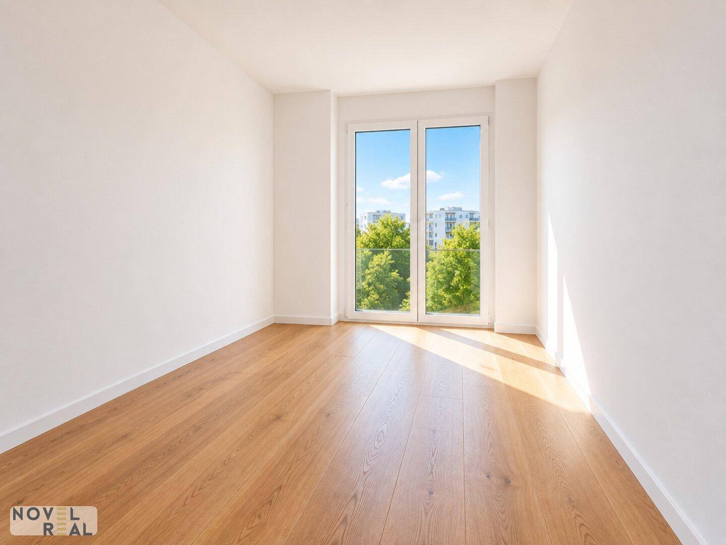 Ruhiges Zimmer mit Holzboden und einem großen Fenster, das viel Sonnenlicht und Grünblick bietet.