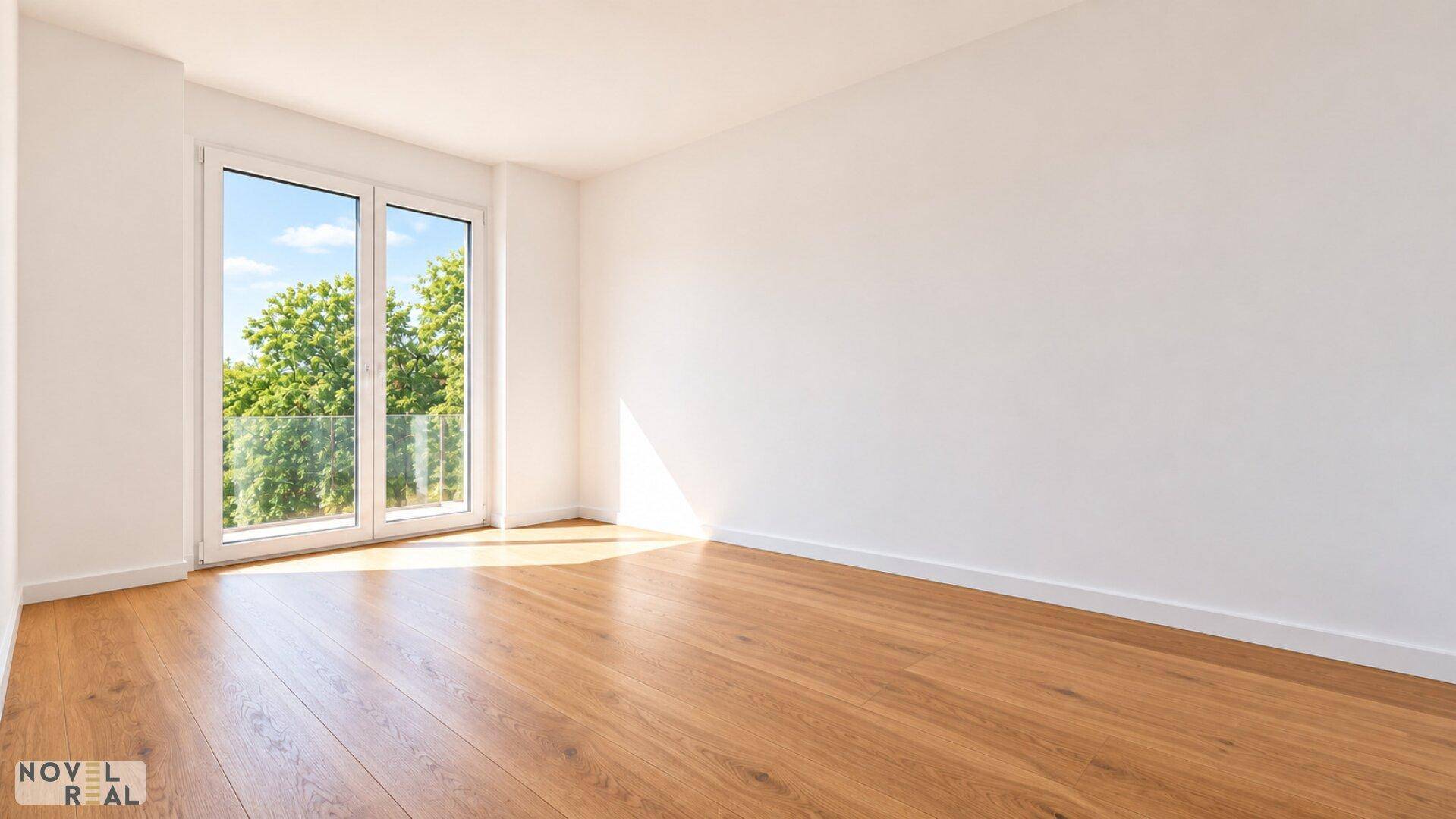 Helles Zimmer mit Holzboden und einem Fenster, das den Blick auf Bäume und den Himmel freigibt.