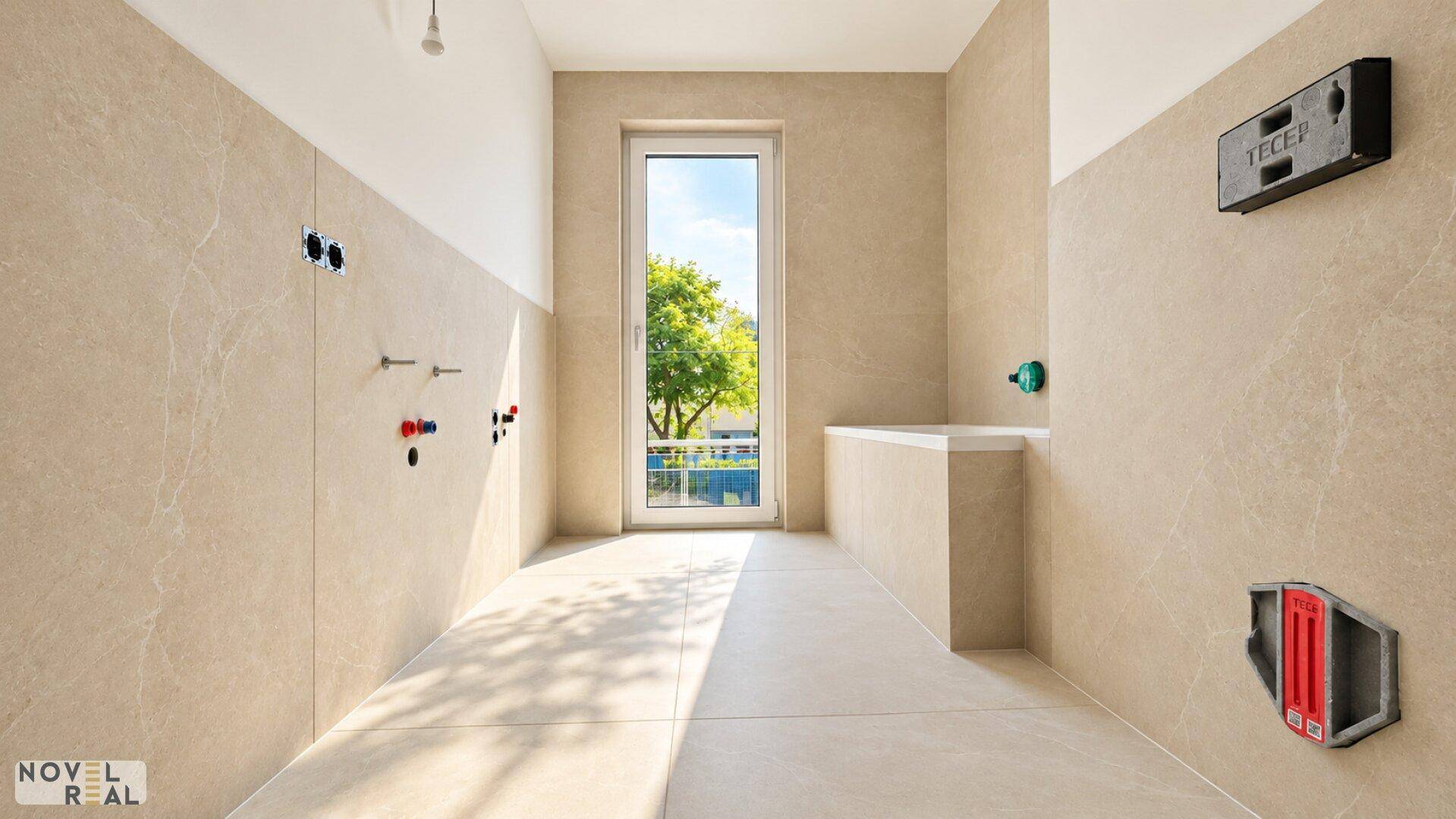 Modernes Badezimmer mit beigefarbenen Fliesen, Fenster und Vorinstallationen für Badewanne und WC.