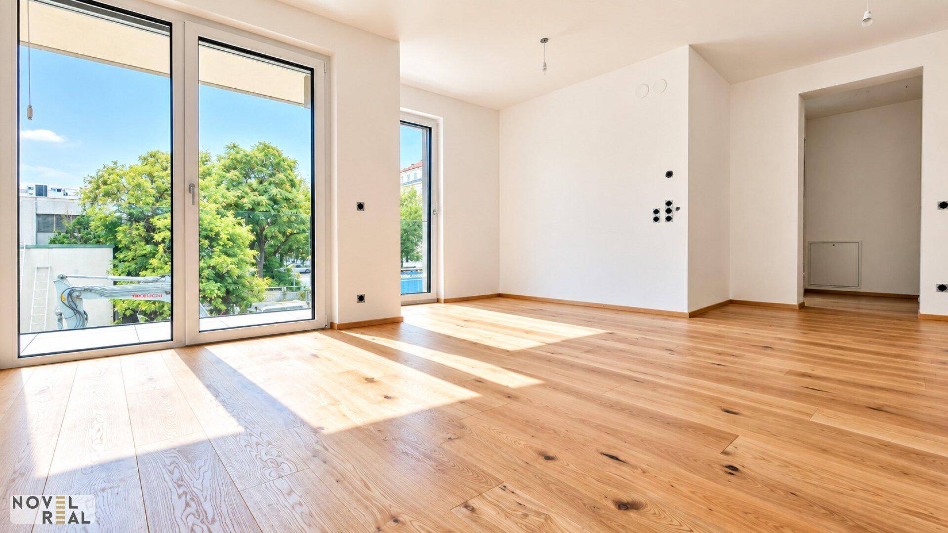 Lichtdurchfluteter Raum mit Holzboden und großen Fenstern, die einen Blick ins Grüne ermöglichen.