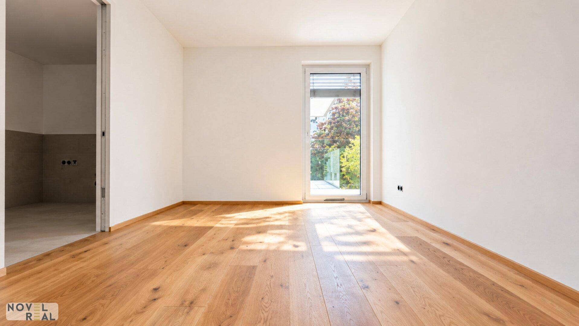 Leerer Raum mit Holzboden und einer Tür, die zu einem Balkon oder einer Terrasse führt.