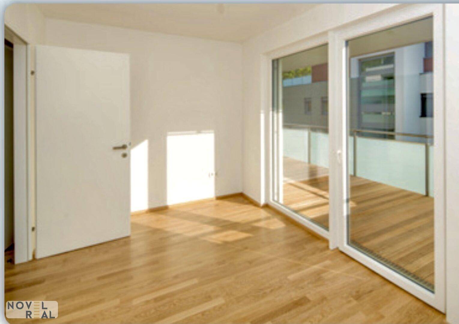 Heller, leerer Raum mit Holzboden und Zugang zu einem Balkon, durchflutet von Sonnenlicht.