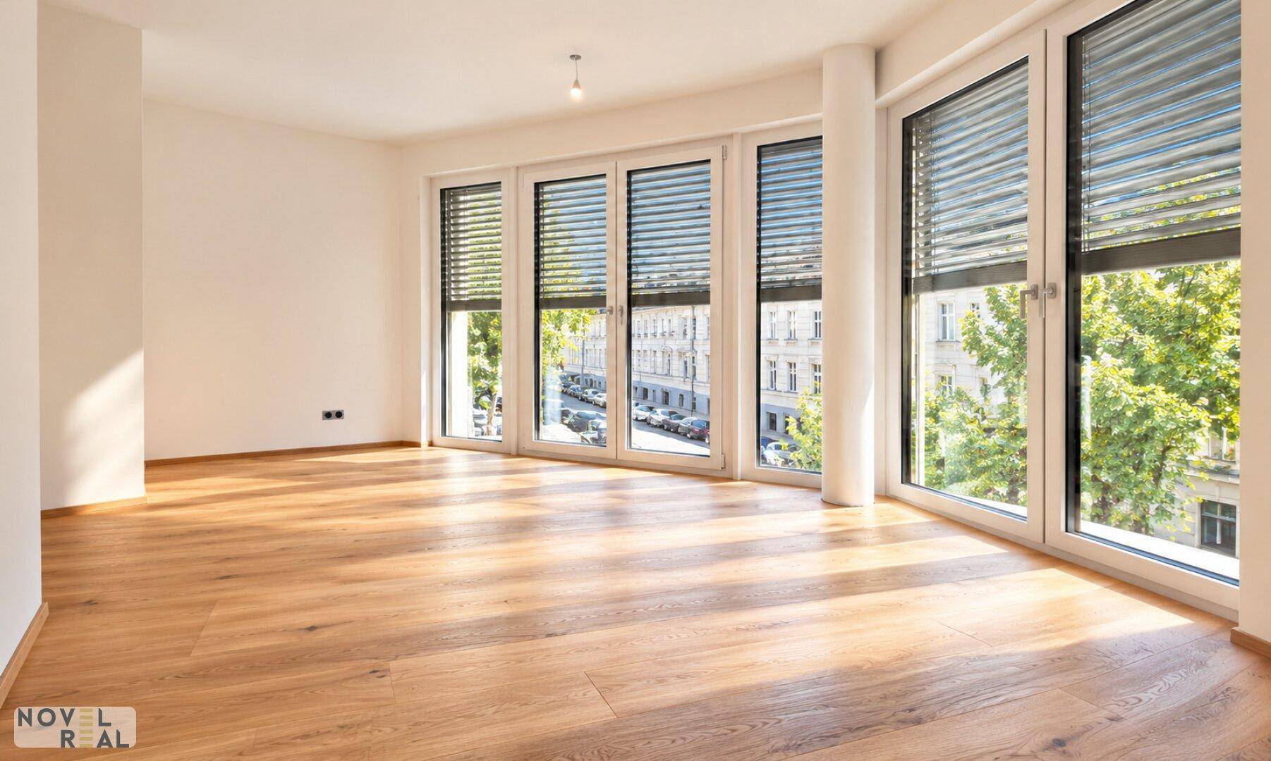 Geräumiges Wohnzimmer mit Holzboden und großen Fenstern, die viel Tageslicht hereinlassen.
