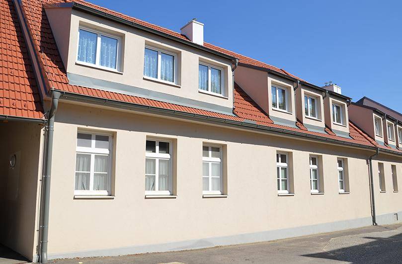 Seitenansicht eines Gebäudes mit beiger Fassade, roten Ziegeldächern und mehreren Dachgauben.