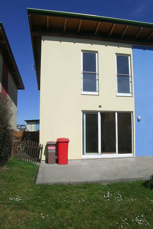 Seitenansicht eines modernen Reihenhauses mit kleiner Terrasse und Zugang zum Garten.
