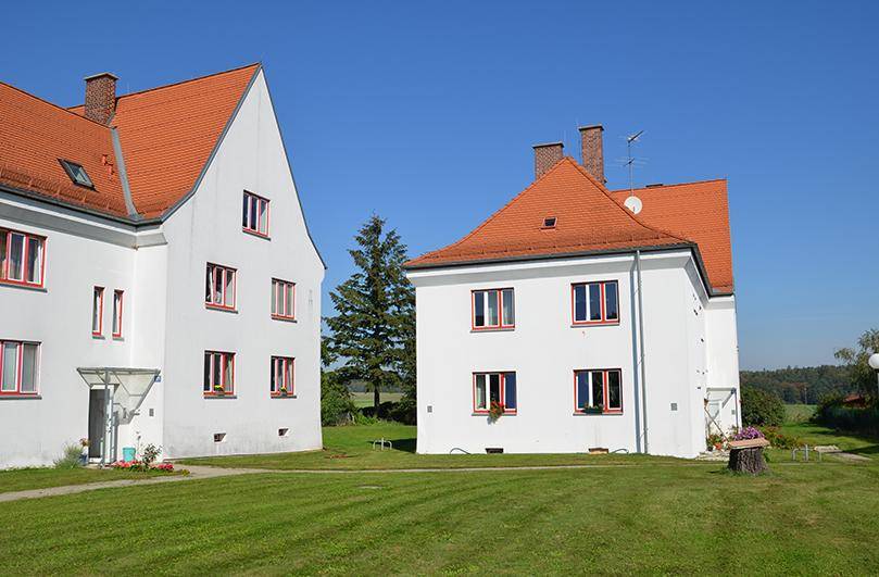 Zwei traditionelle weiße Gebäude mit roten Dächern, umgeben von einer weitläufigen grünen Wiese.