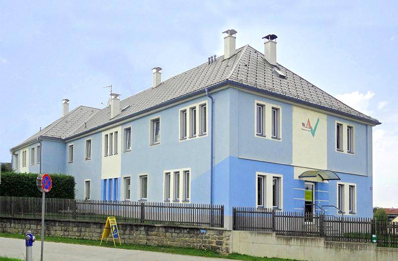 Vorderansicht des modernen Gebäudes mit hellblauer Fassade und Eingangsbereich.