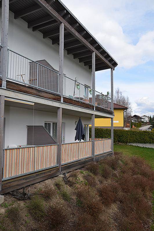 Seitenansicht einer modernen Wohnanlage mit gestuften Balkonen und Terrassen, umgeben von grüner Vegetation.