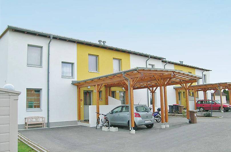 Reihenhäuser mit gelb-weißer Fassade und überdachten Stellplätzen für Fahrzeuge.