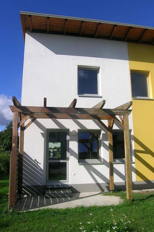 Eingangsbereich eines Reihenhauses mit weißer Fassade und einer Holzpergola.