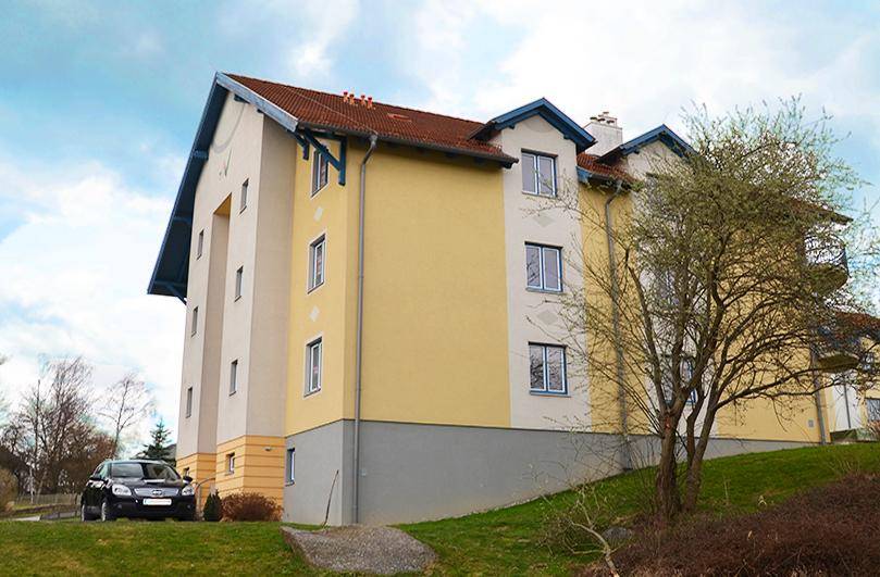 Wohngebäude mit gelber Fassade, rotem Dach und einem geparkten Auto auf dem Grundstück.
