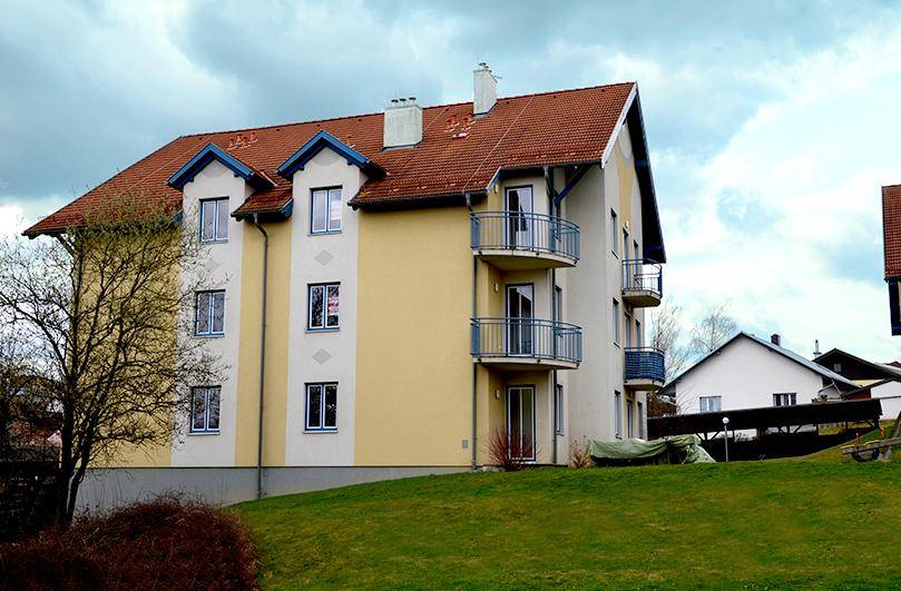 Seitenansicht des Wohnhauses mit roten Ziegeln, Balkonen und grüner Umgebung.