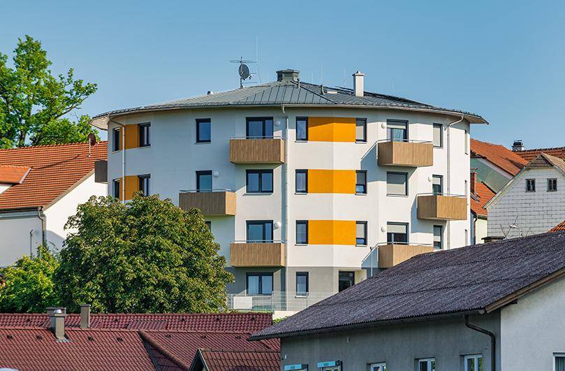 Modernes, rundes Wohngebäude mit orangefarbenen Akzenten und Balkonen unter blauem Himmel.