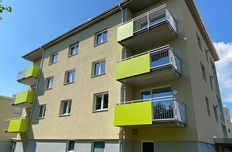 Nahaufnahme der modernen Fassade eines Wohnhauses mit hellgelbem Putz und leuchtend grünen Balkonen unter blauem Himmel.