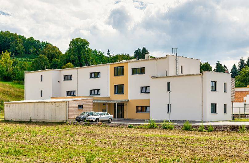 Modernes Wohngebäude in ländlicher Umgebung mit Parkplätzen und angrenzenden Feldern.
