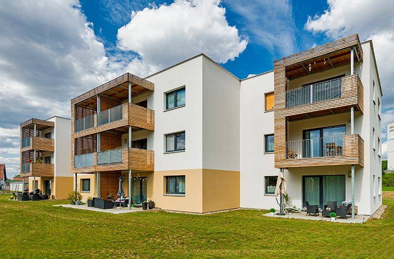 Moderne Wohngebäude mit Terrassen und Balkonen, umgeben von einer grünen Rasenfläche.