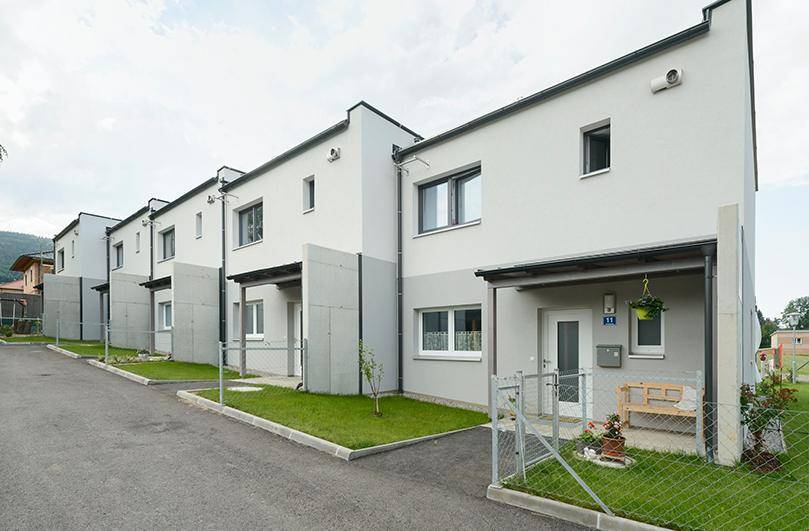 Moderne Reihenhäuser mit heller Fassade und kleinen Vorgärten an einer Zufahrtsstraße.