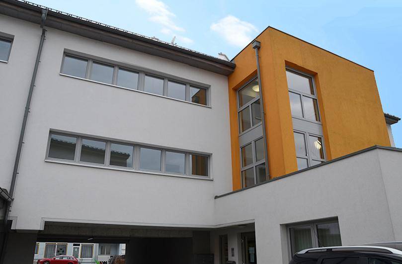 Moderne Architektur des Gebäudes mit großen Fenstern und gelben Akzenten unter leicht bewölktem Himmel.