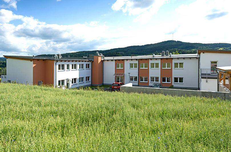 Mehrfamilienhaus in ländlicher Umgebung mit weitem Blick auf grüne Hügel und Wiesen.