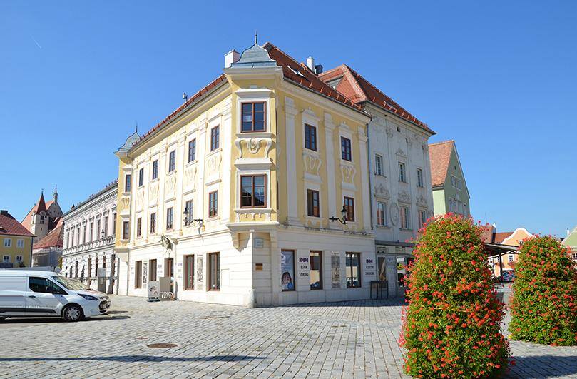 Historisches Gebäude mit gelber Fassade und traditioneller Architektur an einem sonnigen Stadtplatz.