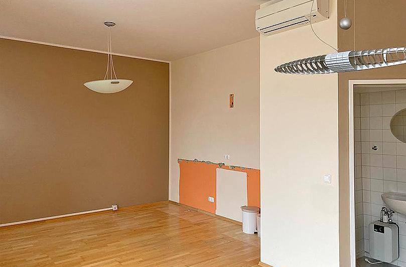Wohnbereich mit Holzboden, Klimaanlage und sichtbaren Vorbereitungen für Renovierungsarbeiten an der Wand.